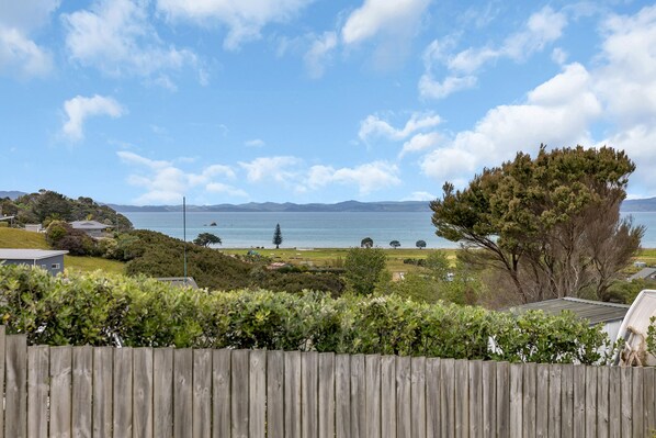 A coastal view with a wooden fence, greenery, and a distant body of water.