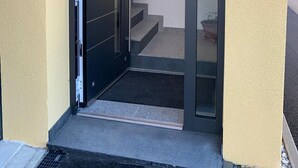 Entrada de un edificio con puerta de cristal, una escalera que conduce al interior y un cartel que indica zona para no fumadores.