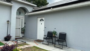 A house with a white exterior, a front door, and a small patio area with two chairs and a table. - Cozy Apartment in S Orlando, approx. 20 minutes away from Disney and Universal. (Orlando)
