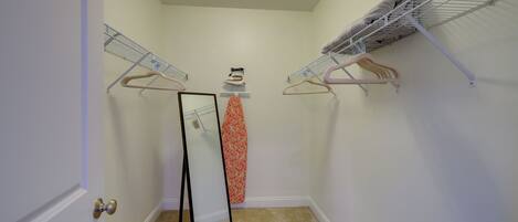 A small, carpeted closet with two metal drying racks, a mirror, and a wall-mounted ironing board.