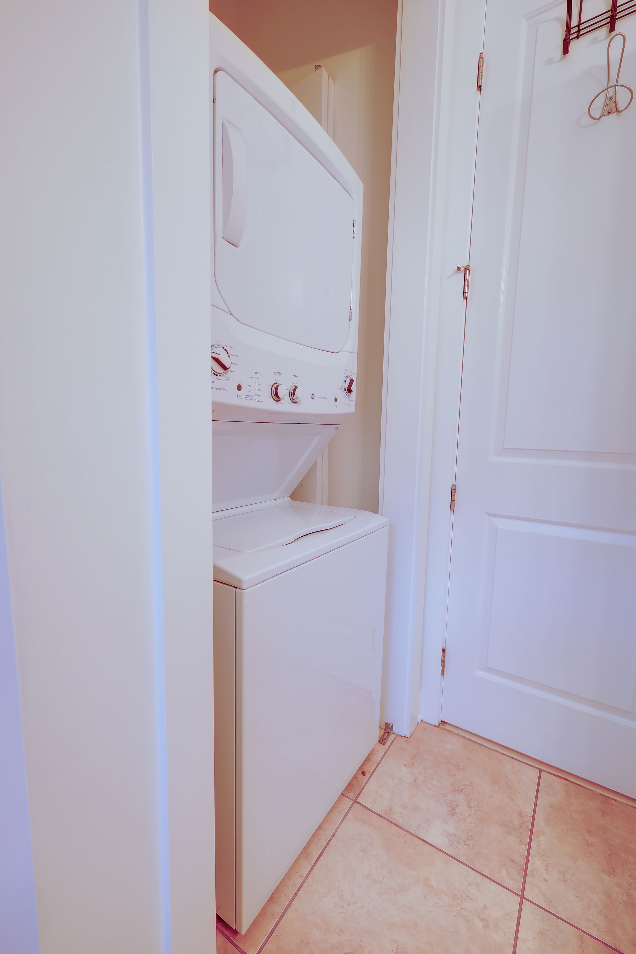Un cuarto de lavado con lavadora y secadora, una puerta con perchero para toallas, y piso de baldosas.