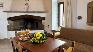 A dining area with a wooden table set for breakfast, a stone fireplace, and a view of the outdoors through a window. - Afroditi 4 bedrooms,pool,Picturesque village (Pigouniana)