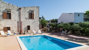 A swimming pool with lounge chairs, a stone building, and a white building in the background. - Afroditi 4 bedrooms,pool,Picturesque village (Pigouniana)