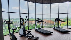 A gym with three treadmills and an elliptical machine, large windows with a city view.