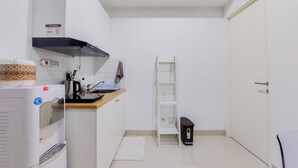 A compact kitchen with a built-in oven, a microwave, and a coffee maker. There is a white shelf unit and a small black appliance on the counter.