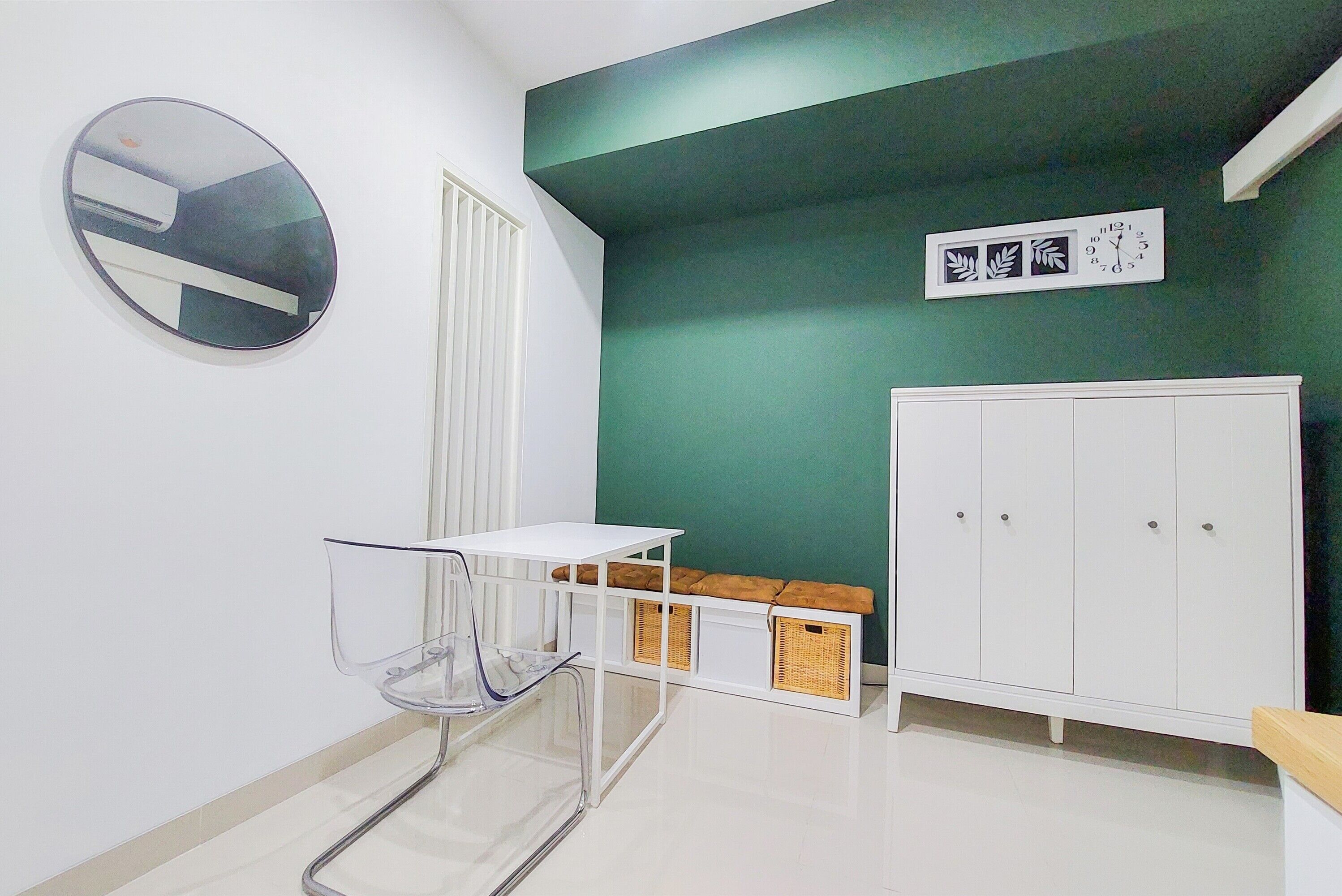 Una habitación con una mesa blanca, una silla transparente, un armario blanco y una pared verde decorativa.