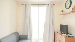 A room with a grey sofa, a wooden cabinet with a TV, and a large window with curtains. - Comfortable And Homey 2Br Belmont Residence Puri Apartment (Jakarta)