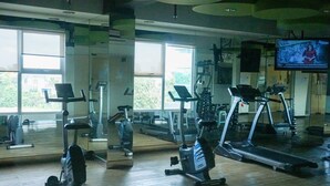 A gym with exercise equipment, large windows, and a TV screen. - Comfortable And Homey 2Br Belmont Residence Puri Apartment (Jakarta)