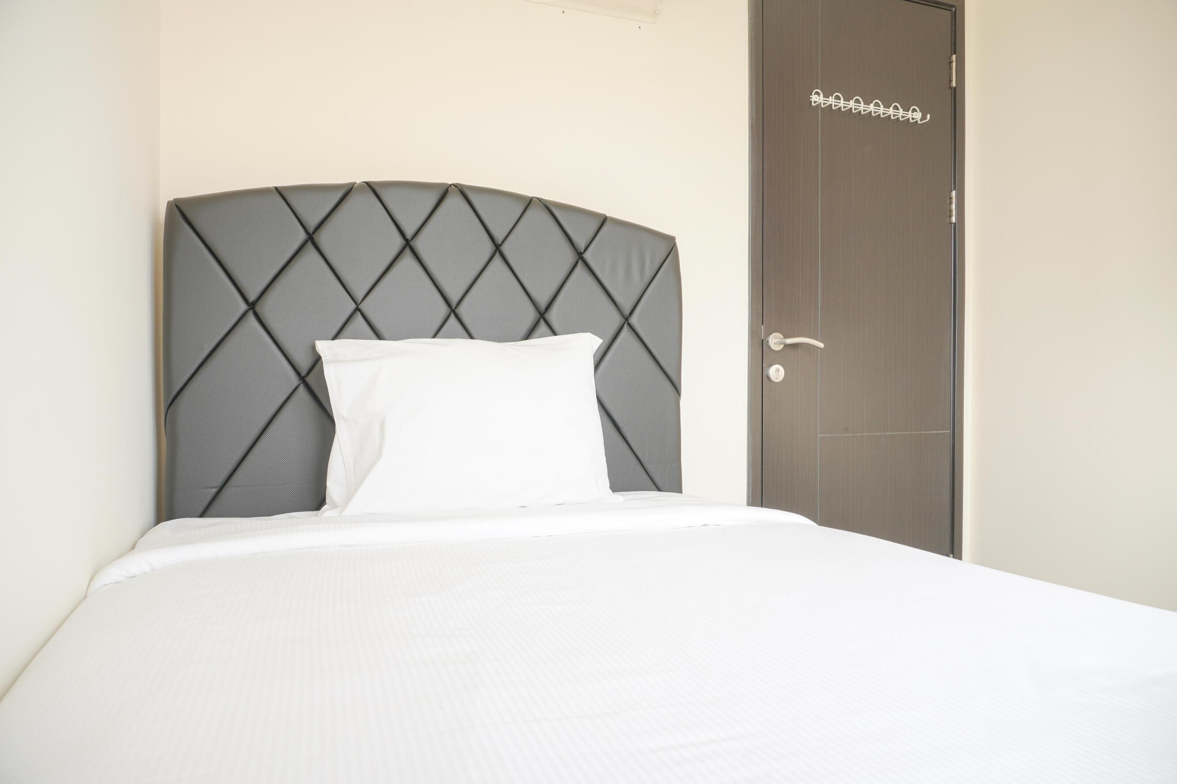 A neatly made bed with a grey headboard in a hotel room.