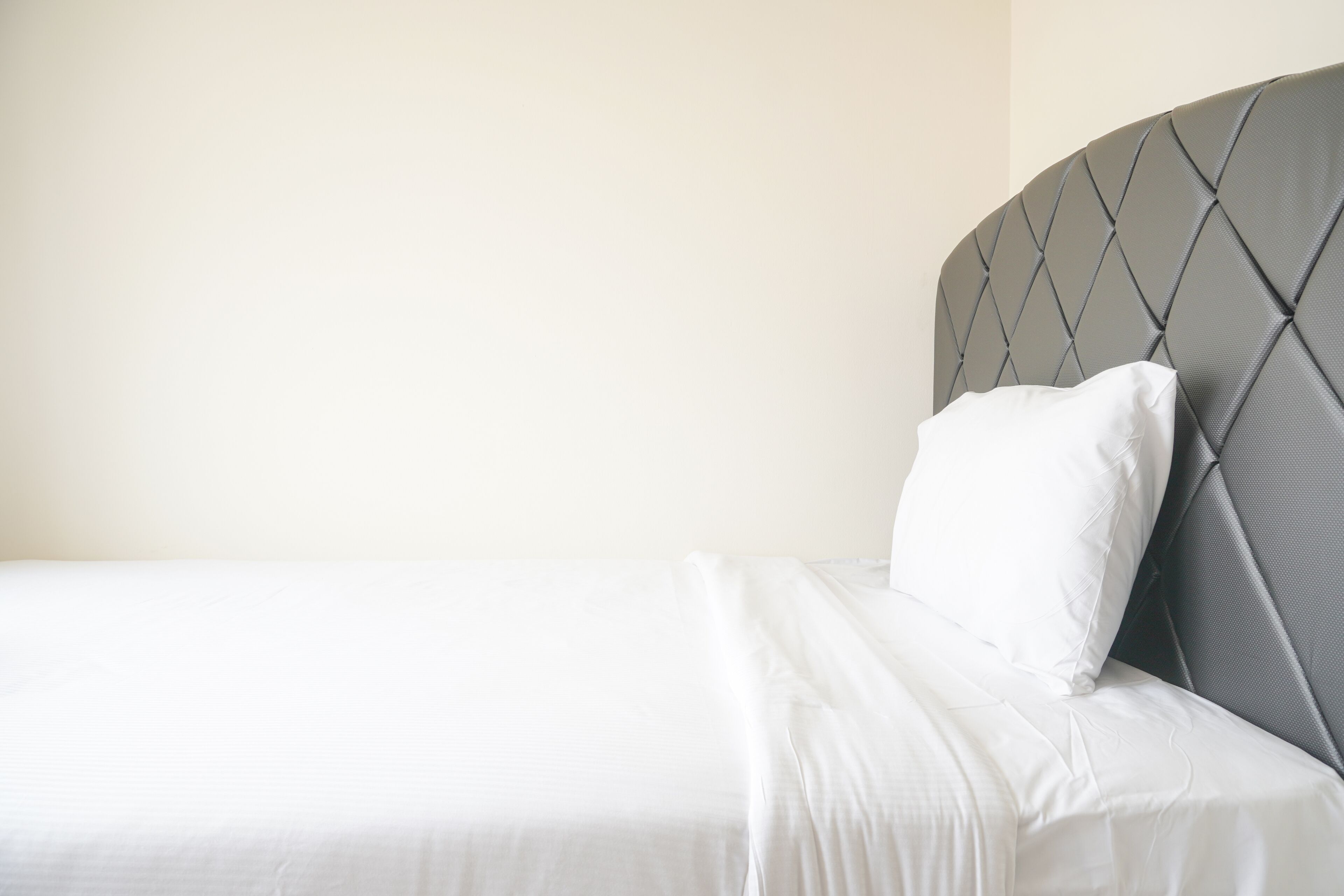 A neatly made bed with a grey upholstered headboard and white bedding.