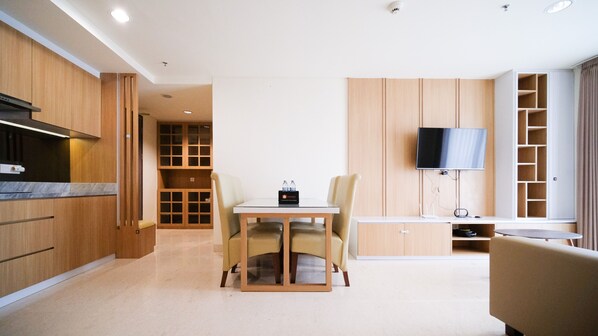 Une chambre d’hôtel moderne dotée d’un coin cuisine, d’une table à manger avec des chaises, d’un téléviseur à écran plat fixé au mur et d’un coin salon avec un canapé.