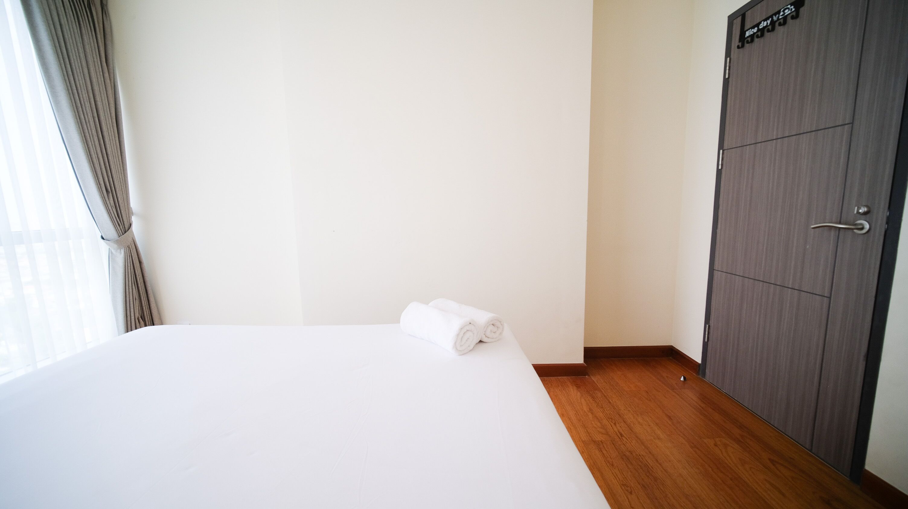 Een hotelkamer met een net opgemaakt bed, een houten vloer, een kledingkast en een raam met gordijnen.