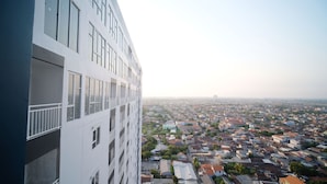 A high-rise building with multiple floors and balconies, overlooking a densely populated urban area with various buildings and streets. - Tidy And Cozy Stay Studio Apartment At Suncity Residence (Sidoarjo)