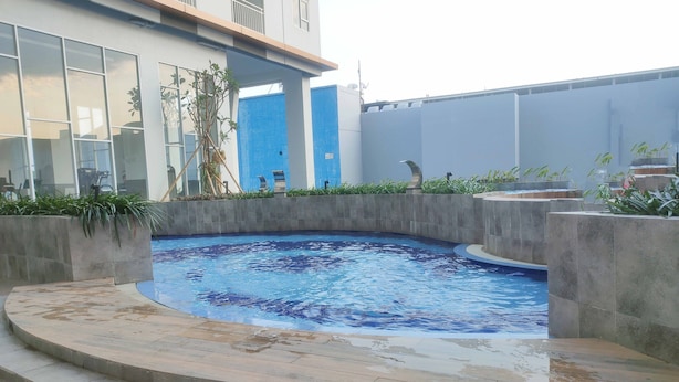 A swimming pool with a curved edge, surrounded by a low stone wall and steps leading into the water. - Tidy And Cozy Stay Studio Apartment At Suncity Residence (Sidoarjo)
