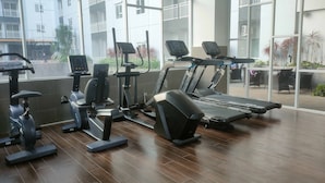 A gym with exercise equipment, large windows, and a view of a building outside. - Tidy And Cozy Stay Studio Apartment At Suncity Residence (Sidoarjo)