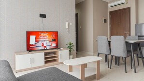 A modern living room with a flat-screen TV, a dining area with chairs and a table, and a small plant.
