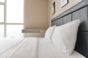 Uma cama bem arrumada com lençóis brancos em um quarto com uma janela grande, uma prateleira fixada na parede e um quadro emoldurado.