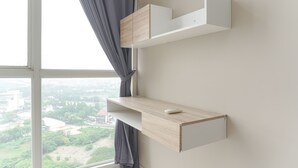 A room with a large window, a white desk with a computer mouse, and a wooden cabinet.