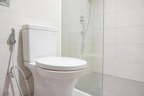 Ein modernes Badezimmer mit Toilette in Weiß, einer Duschkabine aus Glas und einer sichtbaren Dusche.
