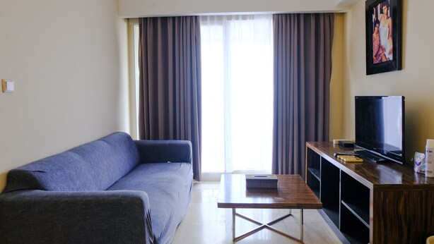A living room with a sofa, a coffee table, a TV, and a painting on the wall. - Strategic And Comfortable 2Br At Braga City Walk Apertment (Bandung)