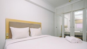 Een netjes opgemaakt bed met witte lakens en kussens, een houten hoofdbord en een opgerolde handdoek aan de zijkant.