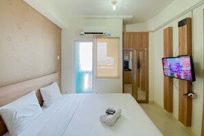 A hotel room with a bed, a TV, and a window with a view of a building. - Comfort Living Studio At 20Th Floor Green Pramuka City Apartment (Jakarta)