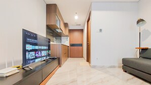 A modern living room with a flat-screen TV displaying a streaming service interface, a sofa, a lamp, and a kitchen area in the background. - Cozy And Elegant 1Br The Smith Alam Sutera Apartment (Tangerang)
