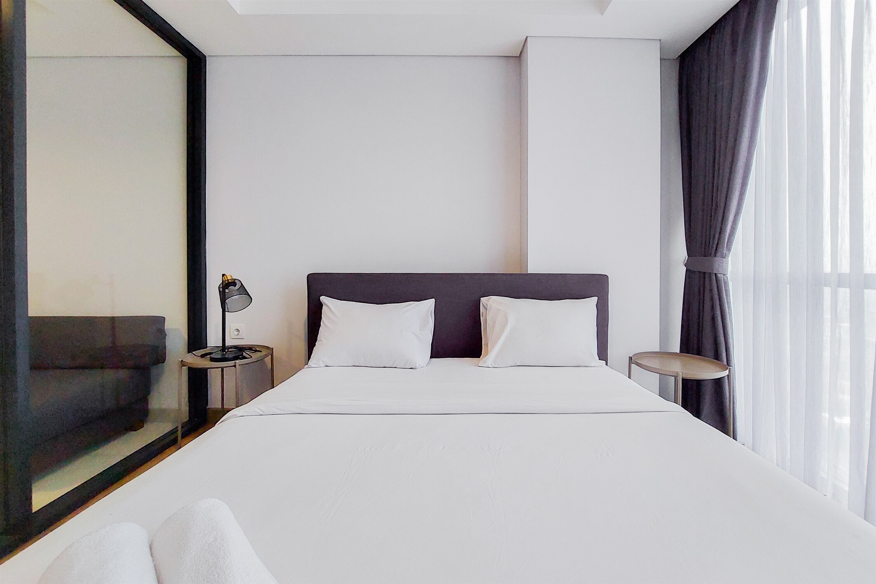 A modern hotel room with a large bed, two bedside tables, and a view of the city through floor-to-ceiling windows.