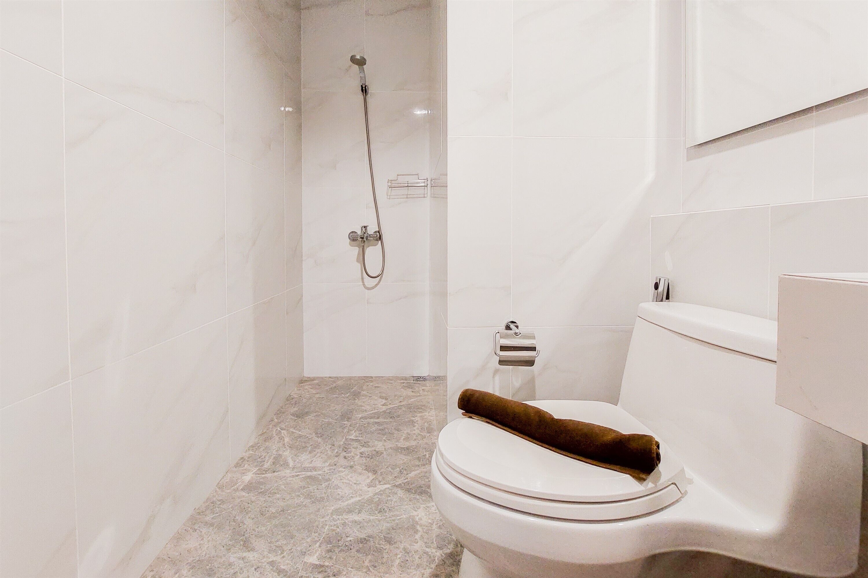 A modern bathroom with a marble floor, a white toilet with a brown towel, and a shower with a handheld showerhead.