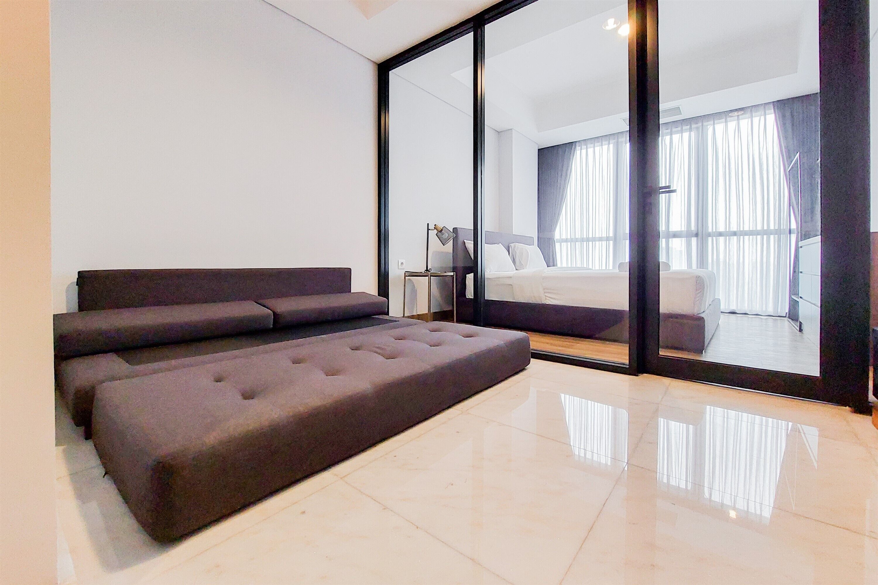 Une chambre d’hôtel moderne dotée d’un grand lit, d’un canapé et d’un mur en verre offrant une vue sur le balcon.