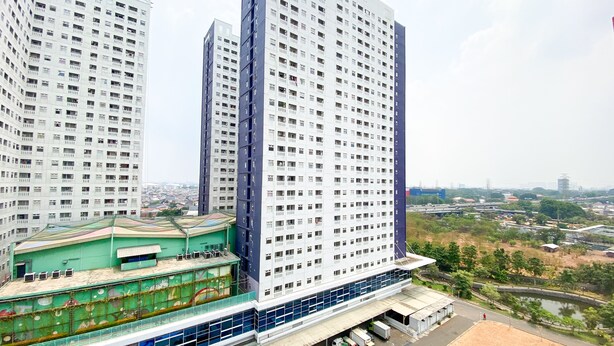 A high-rise building with multiple floors, large windows, and a green-roofed structure at the base.