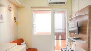 A compact living space with a sofa, a small table, a TV mounted on the wall, and a sliding glass door leading to an outdoor area.