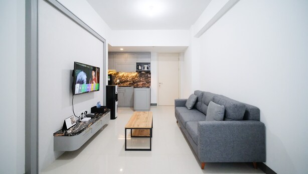 A modern living room with a grey sofa, a coffee table, and a TV mounted on the wall. - Compact And Homey 2Br At Benson Supermall Mansion Apartment (Surabaya)
