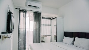 A hotel room with a bed, white bedding, a TV on a stand, and a window with sheer curtains. - Great Deal Studio Serpong Garden Apartment (Cisauk)