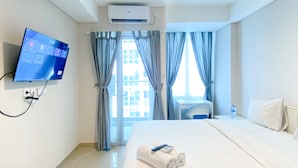 A hotel room with a bed, a desk, a TV mounted on the wall, and an air conditioning unit. - Good Deal And Elegant Studio Tamansari Iswara Apartment (Bekasi)