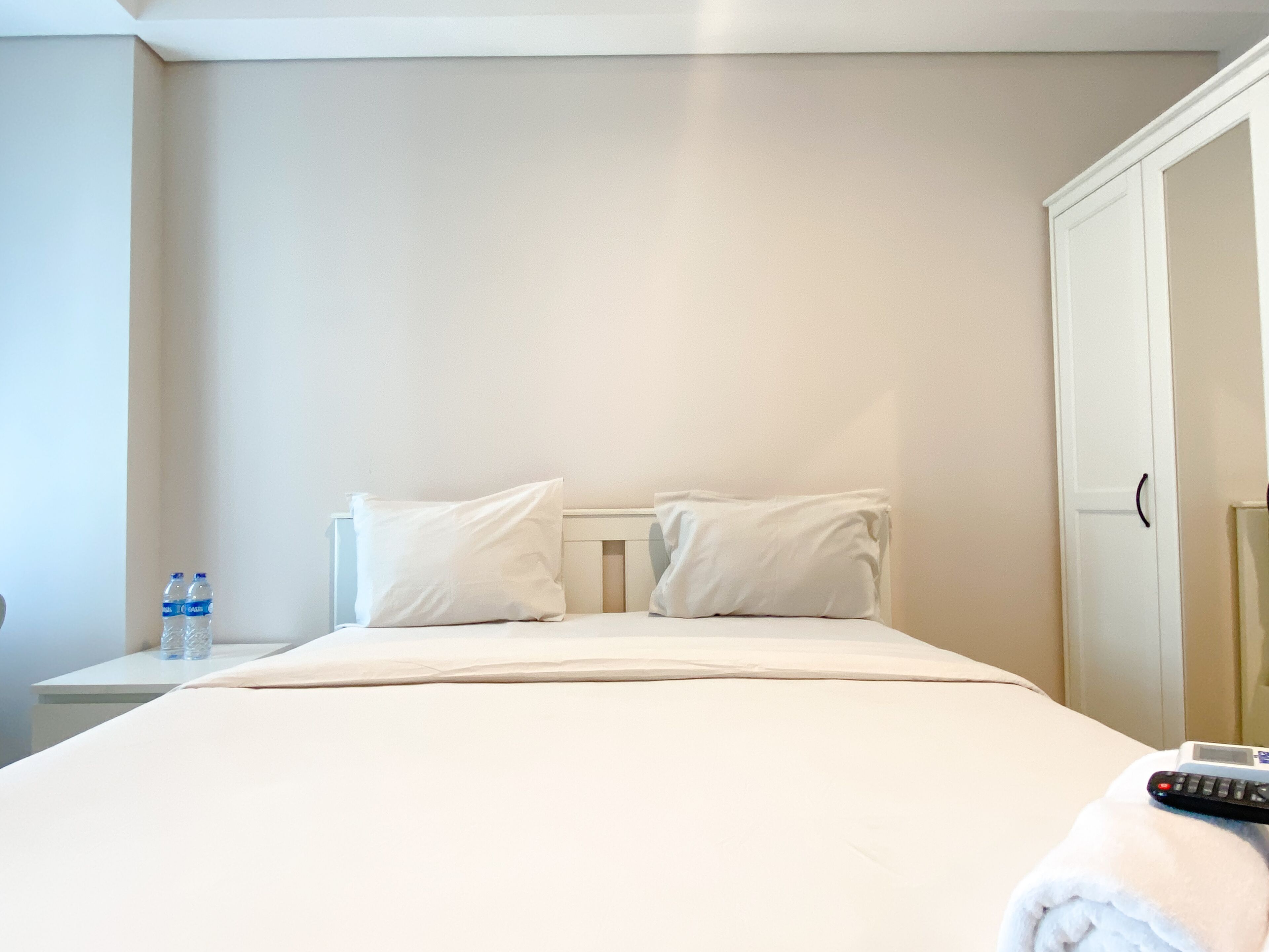 Habitación de hotel con cama, almohadas, mesita de noche con botellas de agua, control remoto y una puerta.
