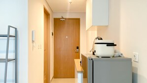 A narrow hallway with a wooden door at the end, a white refrigerator with a coffee maker on top, and a metal ladder leaning against the wall. - Good Deal And Elegant Studio Tamansari Iswara Apartment (Bekasi)