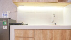 A kitchen with a white countertop, a stainless steel refrigerator, wooden cabinets, and a white tiled backsplash. - Homey And Well Furnished Studio Tokyo Riverside Pik 2 Apartment (Teluknaga)