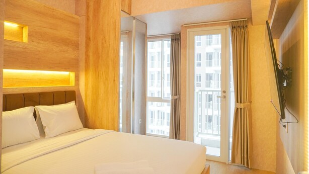 A hotel room with a large bed, wooden headboard, a sliding glass door to the balcony, and a TV mounted on the wall. - Homey And Well Furnished Studio Tokyo Riverside Pik 2 Apartment (Teluknaga)