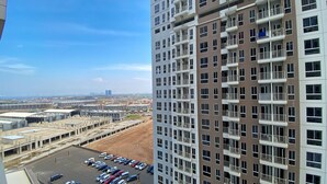 A high-rise building with multiple balconies and a parking lot in the foreground. - Homey And Well Furnished Studio Tokyo Riverside Pik 2 Apartment (Teluknaga)
