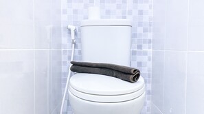 A white toilet with a towel on top, set against a tiled wall. - Fully Furnished Studio At 11Th Floor Tokyo Riverside Pik 2 Apartment (Teluknaga)