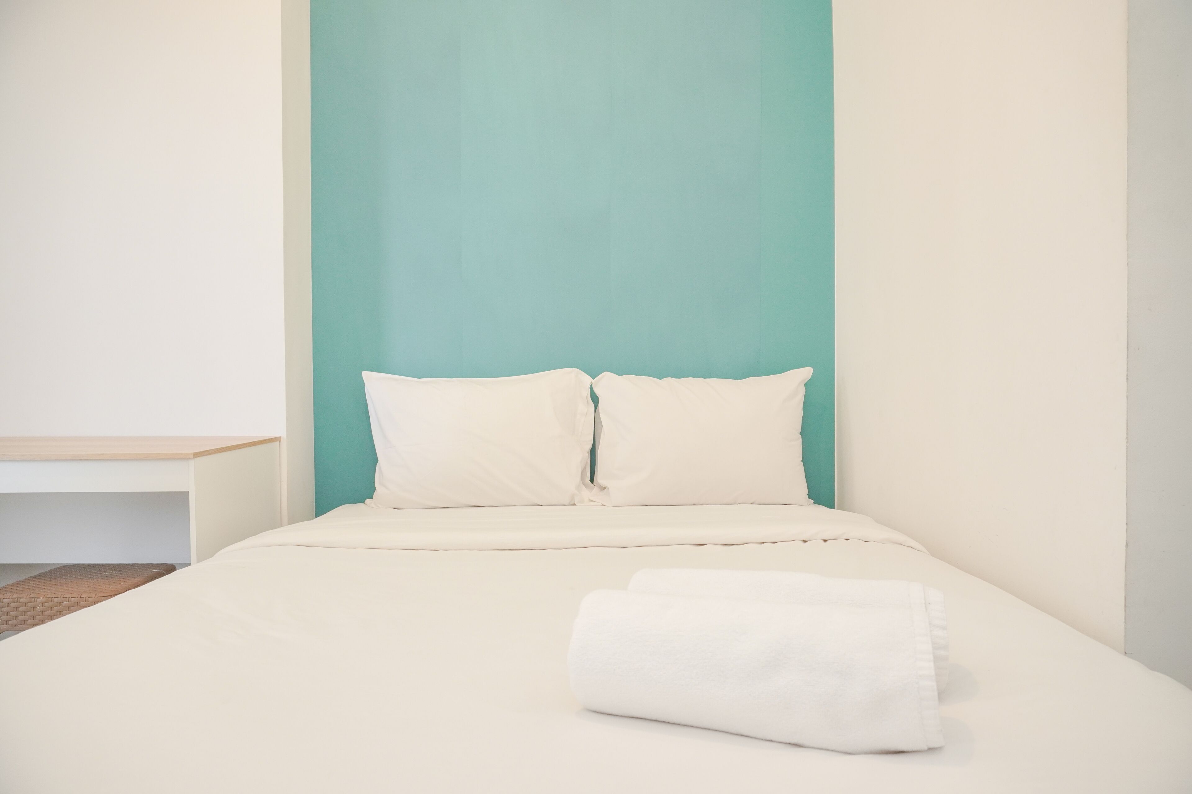 A single bed with white bedding and pillows, a folded white towel, and a wooden nightstand.