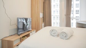 A hotel room with a bed, a TV on a wooden stand, and a window with curtains. - Fully Furnished Studio At 11Th Floor Tokyo Riverside Pik 2 Apartment (Teluknaga)