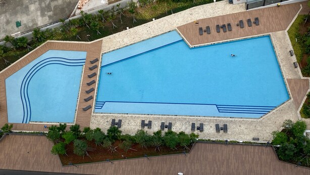 Une vue aérienne d’une grande piscine divisée en plusieurs zones, entourée d’espaces de détente et de verdure.