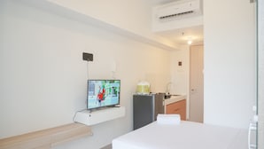 Une chambre d’hôtel avec un lit, un téléviseur fixé au mur, une petite kitchenette et une salle de bain visible à travers une porte ouverte.