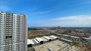 Un immeuble de grande hauteur, doté de nombreux étages et de balcons, une vaste zone industrielle avec des entrepôts et des chantiers de construction, et un ciel bleu dégagé.