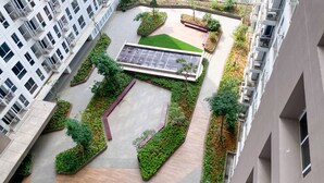 Vista aérea de um edifício residencial moderno com um pátio central, áreas verdes, painel solar e um caminho pavimentado.