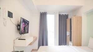 Quarto de hotel com cama, televisão na parede, secretária com computador e guarda-roupa.