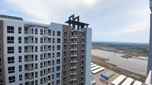 Un edificio de gran altura con varios balcones y una vista de una obra en construcción al fondo.