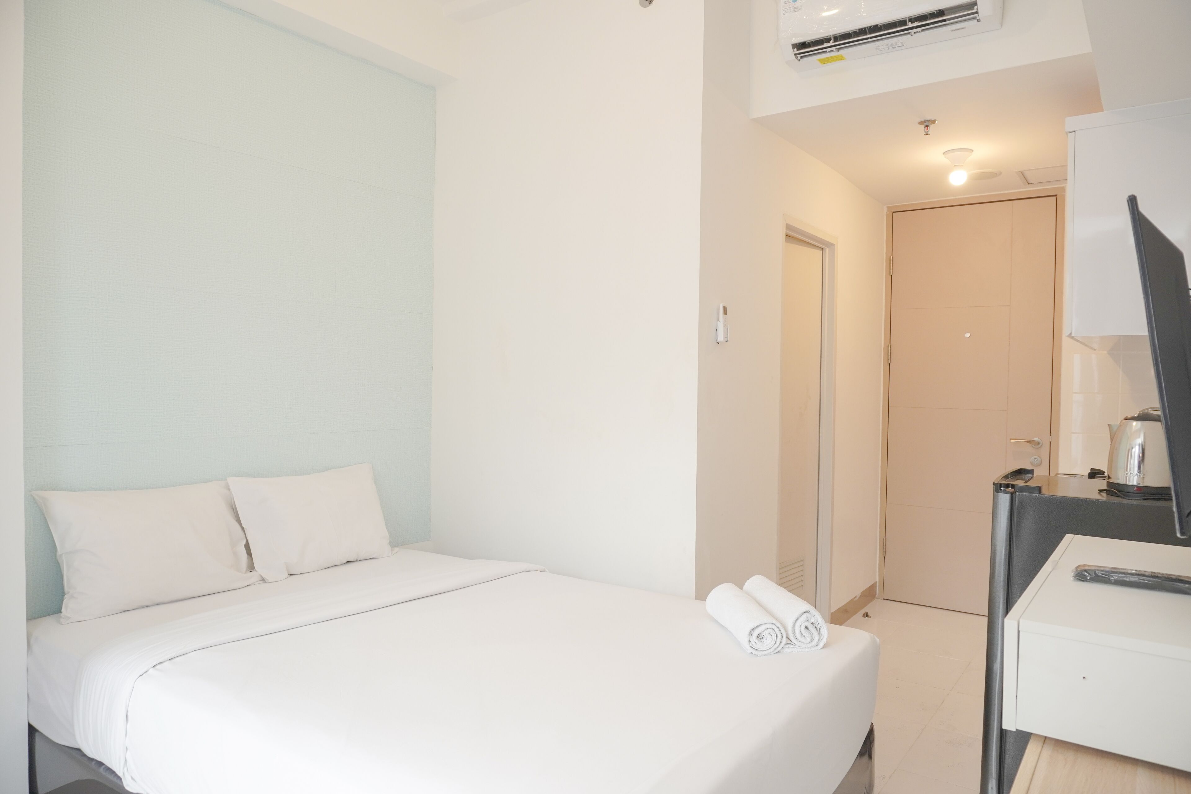 A hotel room with a bed, a desk with a computer, and a door leading to a bathroom.